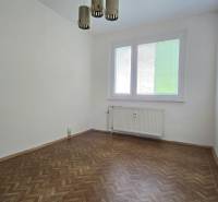 An empty room with a parquet floor, a radiator, and a window in a 3-room apartment.