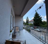 A balcony of a family house in Komárno, overlooking a street with parked cars and trees.
