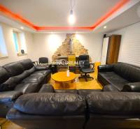 Living room in a family house with black sofas and a stone wall.