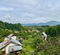 A country cottage in Mojš surrounded by greenery and hills under a blue sky.