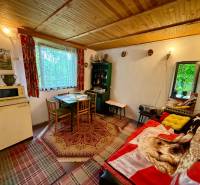 In a cabin with a wooden ceiling, there is a table, chairs, and an antique refrigerator.