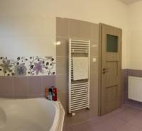 A bathroom in a family house with a wide bathtub, double sink, patterned tiles, and a large mirror.