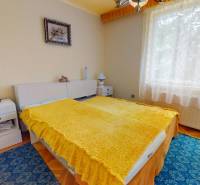 A bedroom with a bed, a yellow blanket, and a painting in a family house.