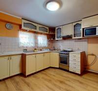 A kitchen in a family house with light cabinets, wooden floor, and orange walls.