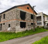 An unfinished family house in Čelovce surrounded by greenery, located by a narrow road.