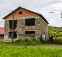 Unfinished family house in Čelovce with grassy surroundings and an adjacent building.