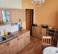A kitchen in a studio apartment with wooden cabinets, a table, and a refrigerator.