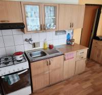 A kitchen in a studio apartment with wooden cabinets and a gas stove.