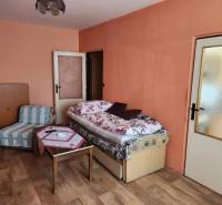 A room in a one-room apartment with a bed, an armchair, and a table on a parquet floor.