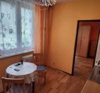 A kitchen in a studio apartment with a table, chairs, and curtains on the window.
