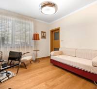 A room in a family house with a sofa, armchairs, a lamp, and wooden flooring.