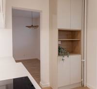 Interior of a 2-room apartment with a white kitchen and wooden shelves.