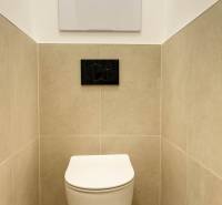 Wall-hung toilet in a 2-room apartment, beige tiles, black flush button.