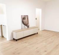 A room in a 2-room apartment with wooden flooring and furniture, next to the kitchen.