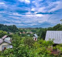 View of cottages in Mojš surrounded by lush greenery and hills under a dramatic sky.