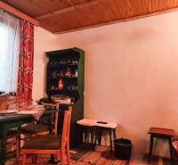 The interior of a cabin with a wooden ceiling, table, chairs, and a shelf.