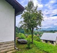 The view from the cottage in Mojš shows roofs, greenery, and distant hills under a cloudy sky.