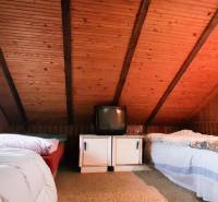 Attic bedroom in a cabin with wooden paneling, beds, and an older television.