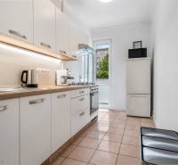 A kitchen with white cabinets, appliances, and a window in a two-room apartment.