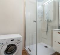 Bathroom in a 2-room apartment with a washing machine, shower, and white tiles.
