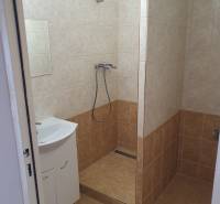 A bathroom of a three-room apartment with a bathtub and a sink, tiled with light ceramic tiles.
