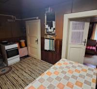 Interior of a cabin with a kitchen, stove, table, and a view into the living area.