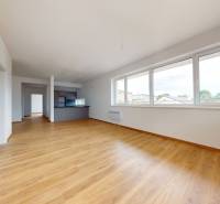 A spacious living room with wooden flooring and large windows in a 3-room apartment.