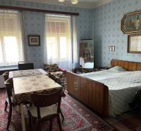 Interior of a family house with a bedroom, table, antique furniture, and decorations on the walls.