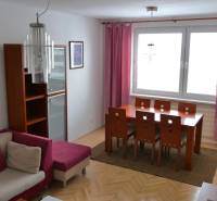 Dining area with a wooden table in a 3-room apartment, complemented by pink curtains and a sofa.