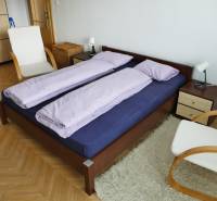 A bedroom in a 3-room apartment with a wooden bed, a chair, and a white carpet.