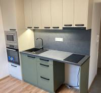 A kitchen in a 3-room apartment with a combination stove and gray cabinets.