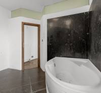 Bathroom with a corner bathtub and black tiles, wooden floor in commercial premises.