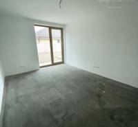 An empty room with a large window in a family house, with an unfinished floor.