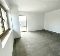 An unfurnished room in a family house with a concrete floor and windows.