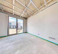 A spacious room in a family house with a large window and an unfinished ceiling.