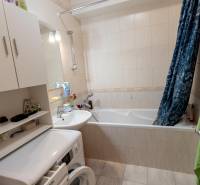 A bathroom in a 4-room apartment with a bathtub, washing machine, and open cabinet.