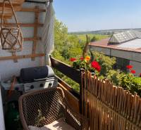 A balcony of a 3-room apartment with seating, a grill, and a view of greenery in Pezinok.