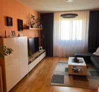 Living room with an orange wall, dark curtains, a large window, and furniture in a three-room apartment.