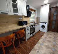 Studio apartment with a kitchenette, washing machine, and wooden chairs.