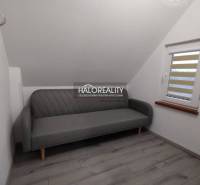 Studio apartment with a slanted ceiling, gray sofa, and window blinds.