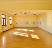 Interior of a building with light walls, wooden floor, and large windows.
