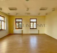 A spacious room with wooden flooring, white walls, and multiple windows in a building.
