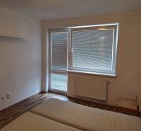 Bedroom in a two-room apartment with a bed and a window with blinds.