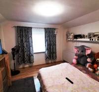 Children's room in a family house with curtains, a bed, a shelf, and stuffed toys.