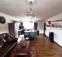 Living room and kitchen in a family house with a sofa, table, and shelves.