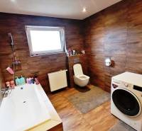 A bathroom in a family house with a bathtub, washing machine, and wooden paneling.