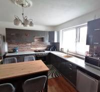 A kitchen in a family house with dark furniture, spacious windows, and a wooden table.