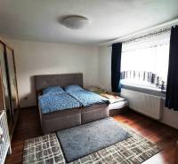 Bedroom in a family house with a bed, cabinet, carpets, and a window with a dark curtain.