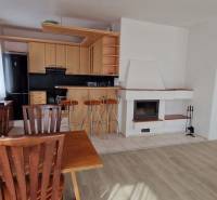 Living room in a family house with a fireplace, kitchen, and wooden furniture.
