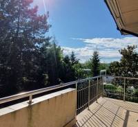 A balcony of a family house with a view of trees, sunny day, open doors.